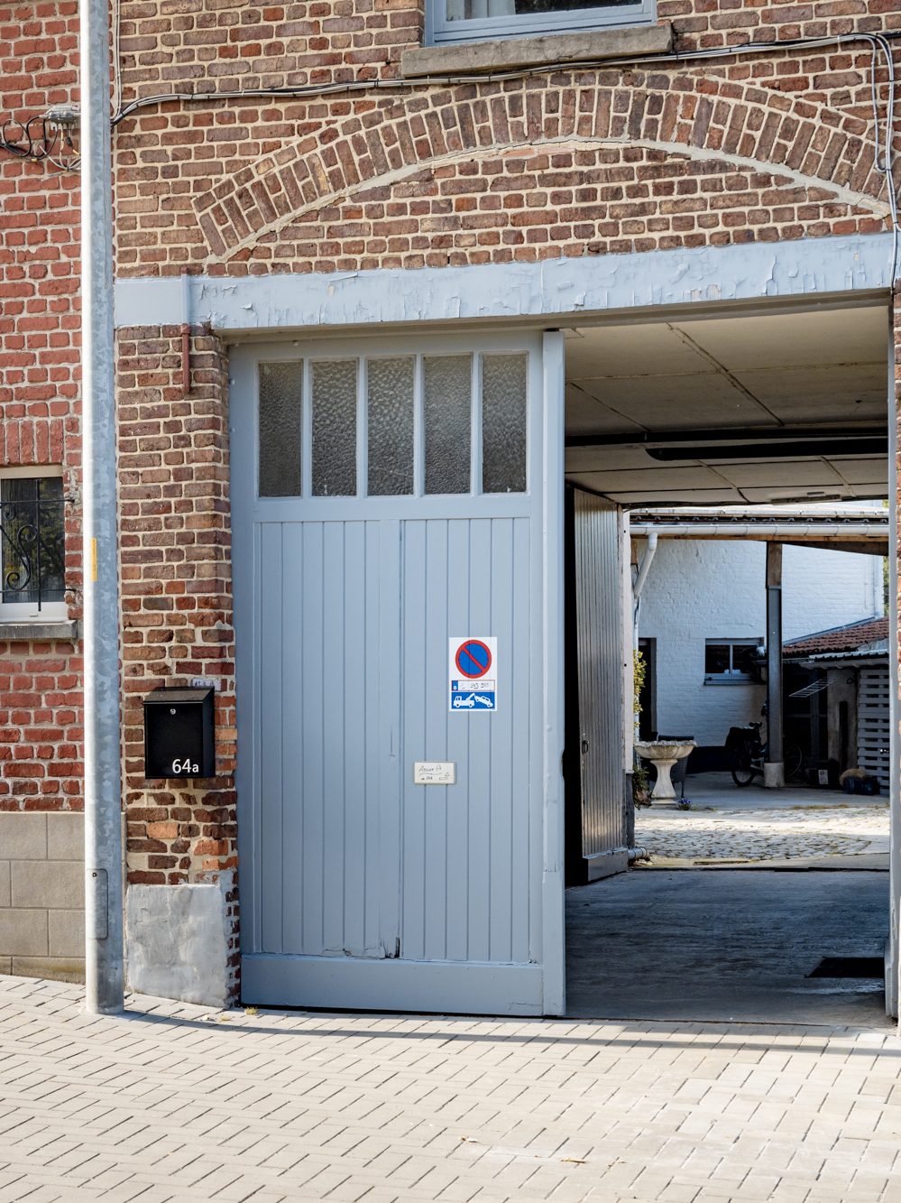 De gevel in de Tweekleinewegenstraat: een bakstenen voorgevel met een lichtblauwe schuurpoort die openstaat.